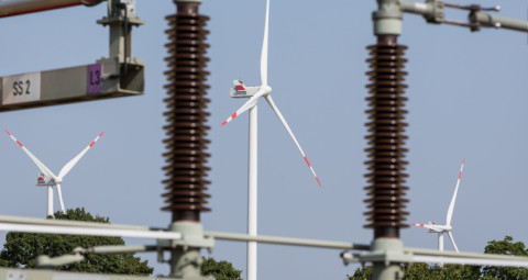 Windkraftanlagen hinter elektrischen Leitungen unter blauem Himmel.
