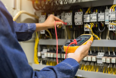 Hand eines Elektrikers, der ein Multimeter an elektrische Anschlüsse anschließt, um Messungen vorzunehmen.