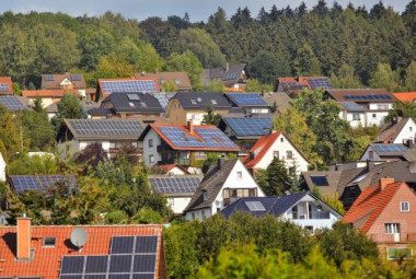 Dachlandschaft mit  Solaranlagen in einem Wohngebiet, umgeben von Bäumen und Grünflächen.