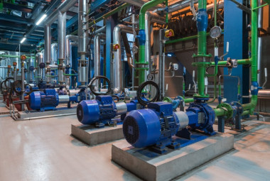 Industrieanlage mit blauen Elektromotoren und grünen Rohrleitungen in einem großen Raum.