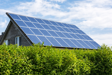 Dach mit Solarpanelen und grüner Hecke unter blauen Himmel.