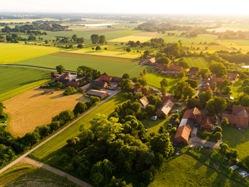 Luftaufnahme einer ländlichen Gegend mit Feldern, Bäumen und einem kleinen Dorf mit roten Dächern.