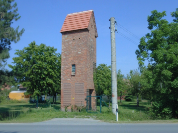 Roter Ziegelturm mit Satteldach und angrenzenden Bäumen in einem grünen Park.