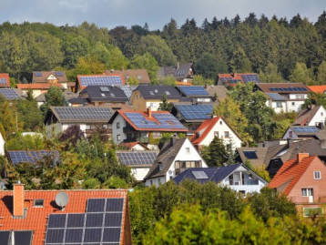 Dachlandschaft mit  Solaranlagen in einem Wohngebiet, umgeben von Bäumen und Grünflächen.