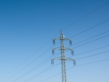 Hochspannungsgleichstrommast mit Seilen vor blauem Himmel.