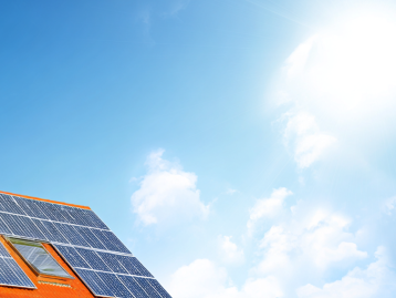 Dach mit Photovoltaikanlagen unter blauem Himmel und strahlender Sonne.