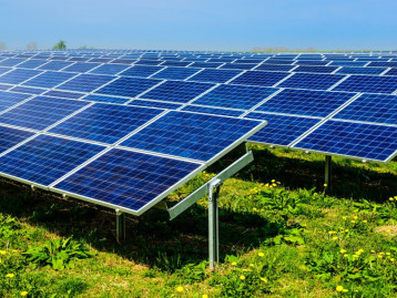 Solaranlage mit Panelen auf einer Wiese, unter blauem Himmel und mit grünem Gras im Vordergrund.