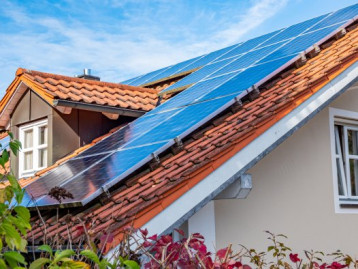 Solaranlage auf dem Dach eines Hauses mit blauen Solarpanelen und einem roten Ziegeldach.