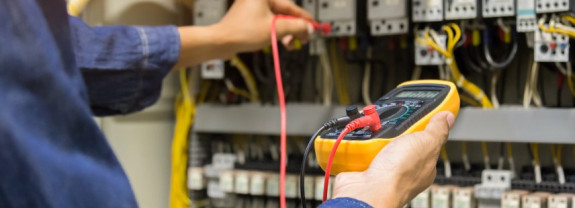 Hand eines Elektrikers, der ein Multimeter an elektrische Anschlüsse anschließt, um Messungen vorzunehmen.