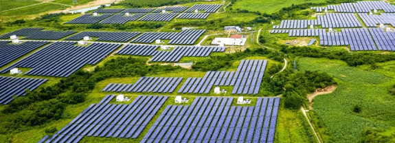 Luftaufnahme eines großen Solarpark mit vielen Solarmodulen in grüner Landschaft.