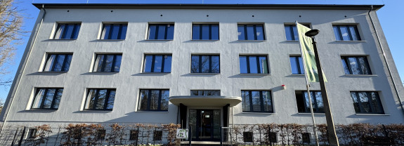Ein helles, modern gestaltetes Gebäude mit mehreren Fenstern und einem Zugang im Vordergrund.