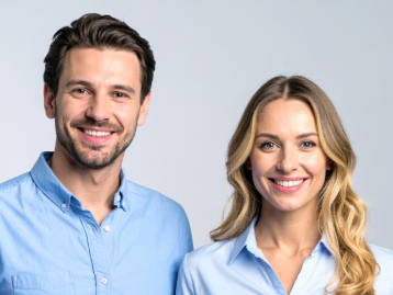Zwei lächelnde Personen in hellblauen Hemden stehen vor einem neutralen Hintergrund.