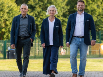 Drei Personen in blauen Blazern gehen auf einem Weg in einem Park.