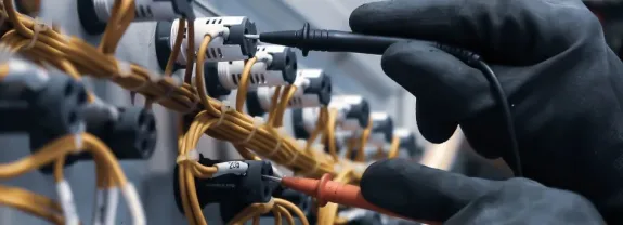 Hand mit Prüfspitzen testet elektrische Anschlüsse und Kabel in einer Schaltanordnung.